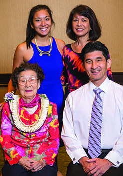 A family of four, two seated and two standing, smile together.