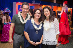 A group of three pose for a photograph at an event, each wearing a lei.