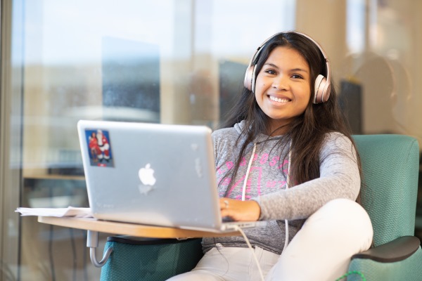 Young girl with headphones on smiling while using a laptop