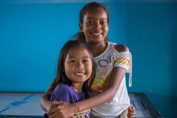 Two young girls smiling and hugging