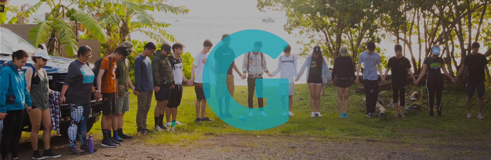 A group gathers, holding hands in a circle. The letter G appears over the image.