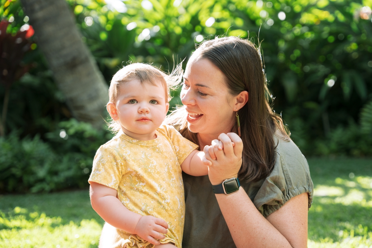 A woman sits with a baby, holding the baby's hand.