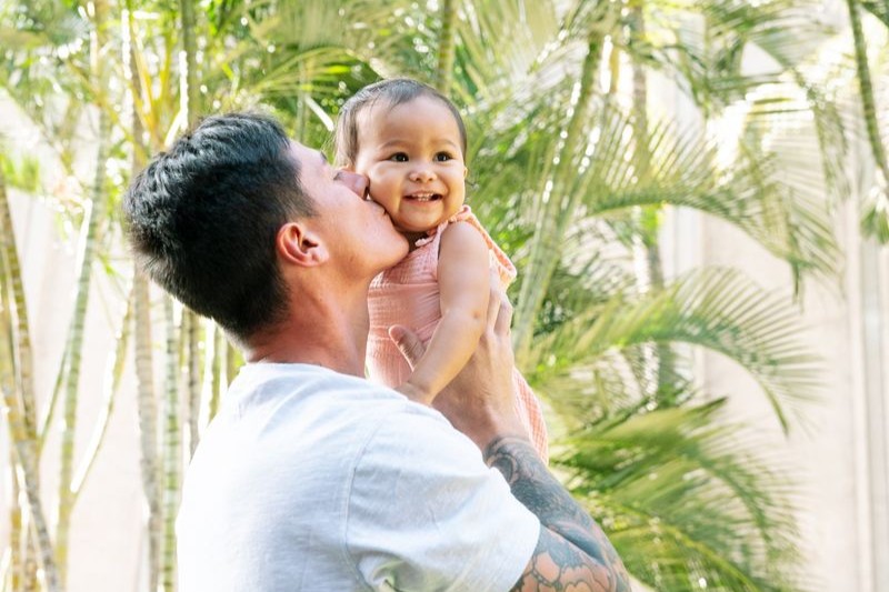 A man holds a baby girl, kissing her cheek.