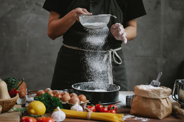 A baker sifts flour into a baking pan.